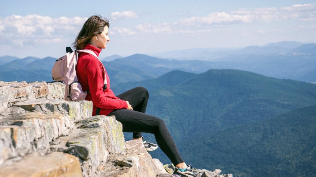 Frau sitzt auf einem Berg und blickt in die Weite als Symbol für Leichtigkeit, Klarheit und neue Energie